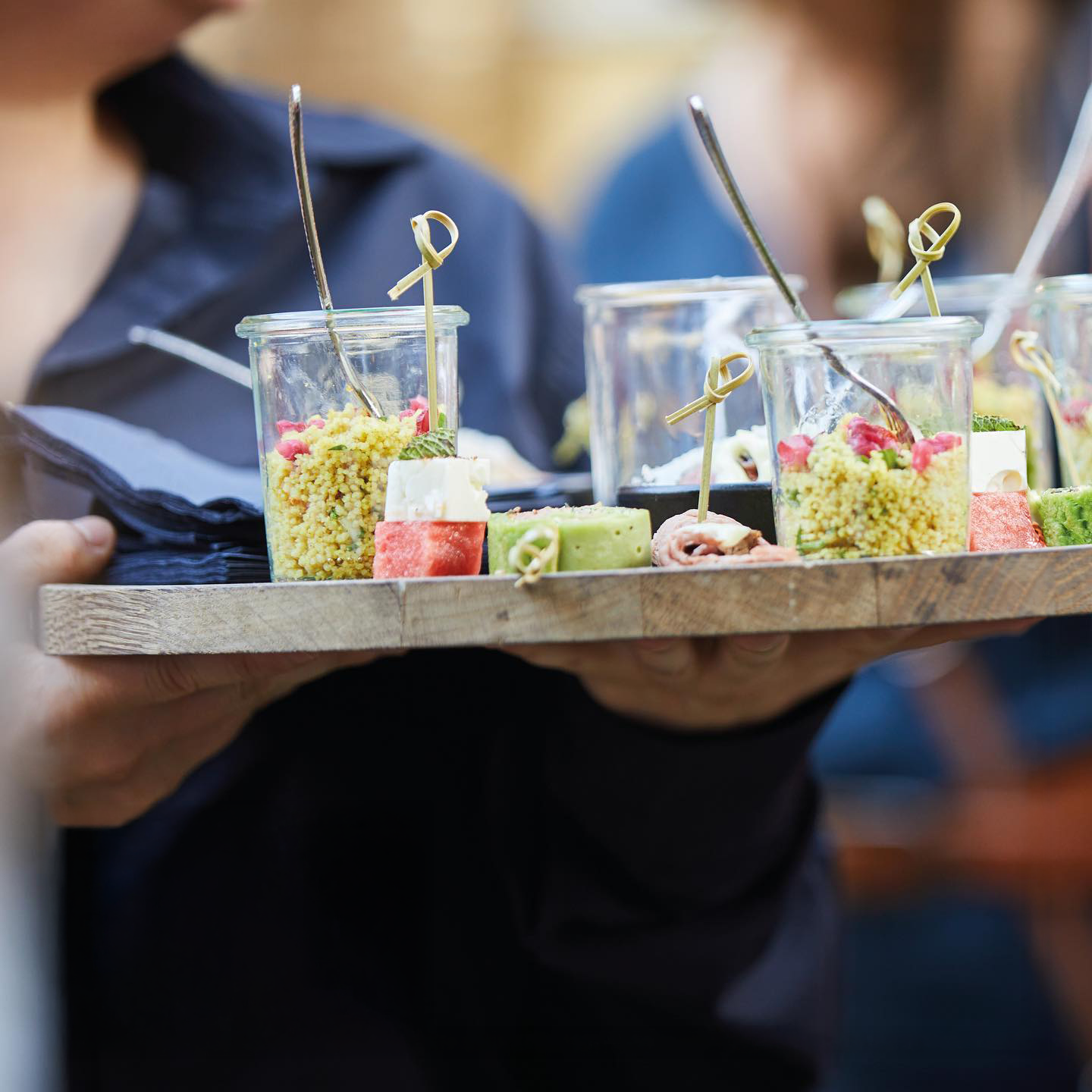 Hand hält Holztablett mit kleinen Gläsern und Fingerfood beim Flying Buffet