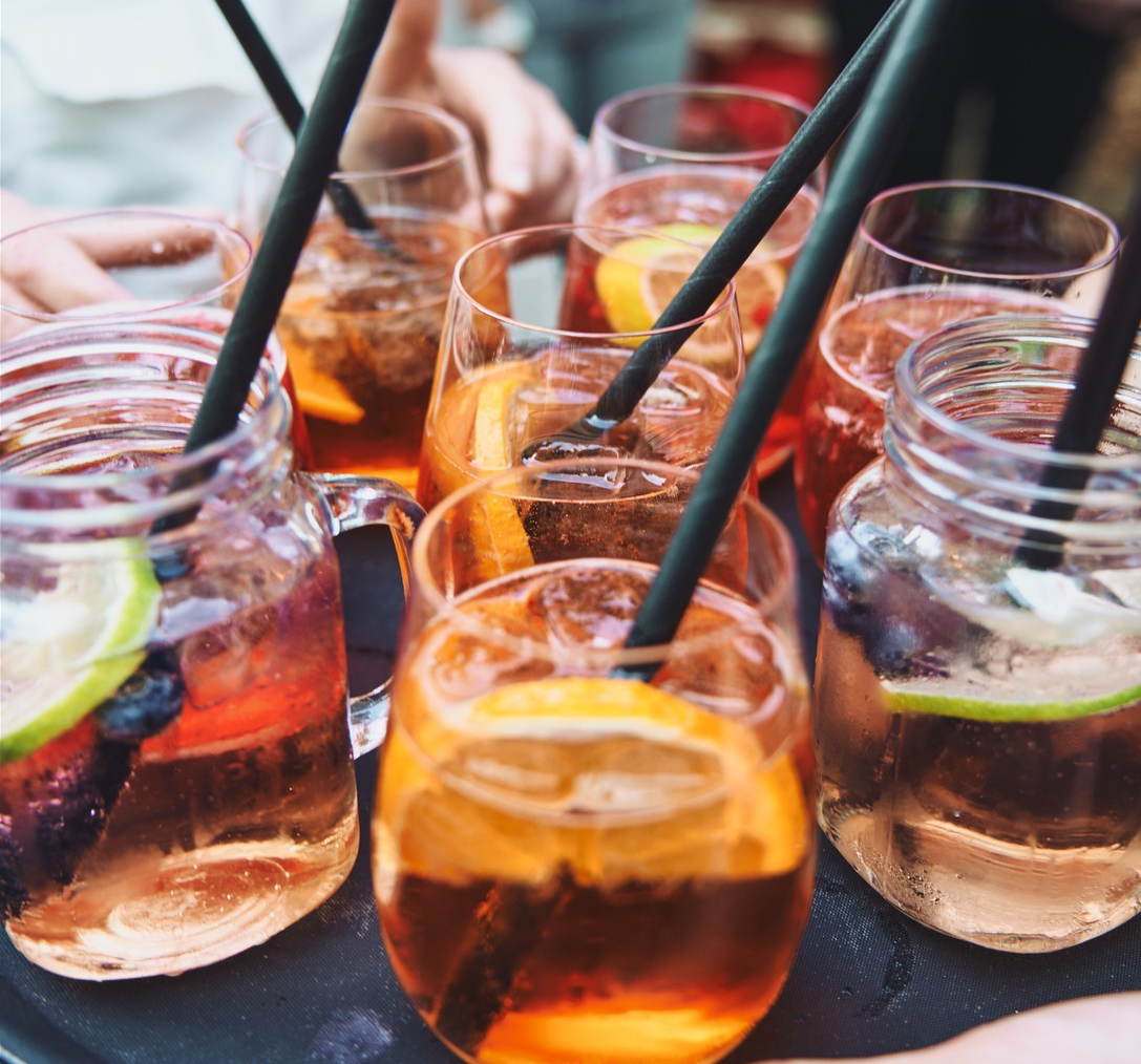 Mehrere Gläser mit bunten Sommerdrinks, Eis und Trinkhalmen